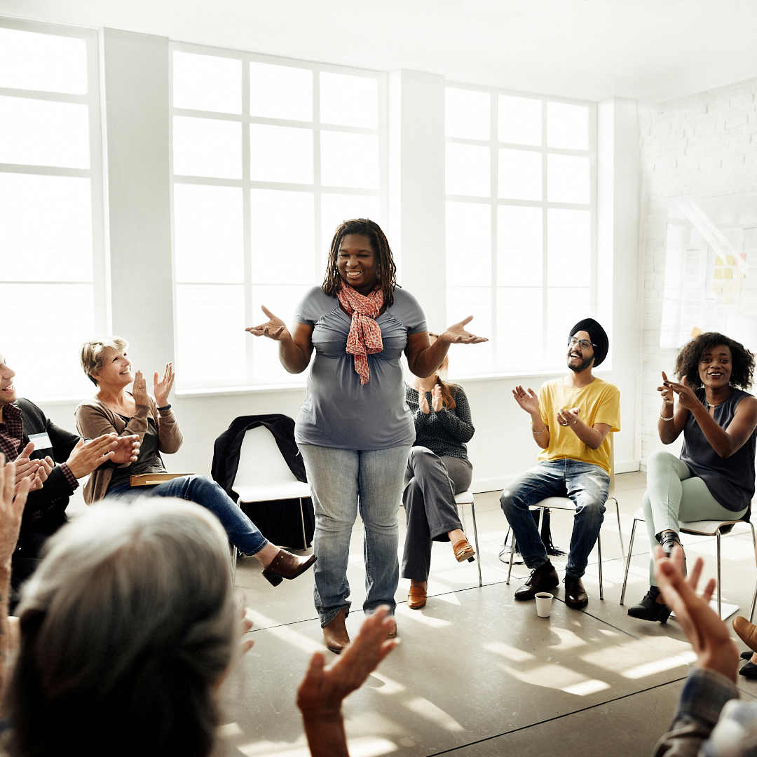 Woman talking to a group of people who are clapping hands. Image used for Group Coaching - Keto Coach
